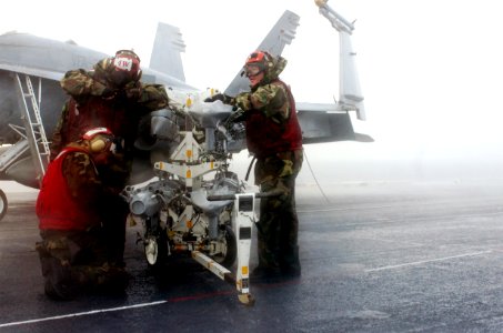 US Navy 070130-N-0555B-189 Braving wind and rain, aviation ordnancemen assigned to Strike Fighter Squadron Two Five (VFA-25) huddle around a bomb rack trying to finish their checks before the rain becomes an impediment to safet