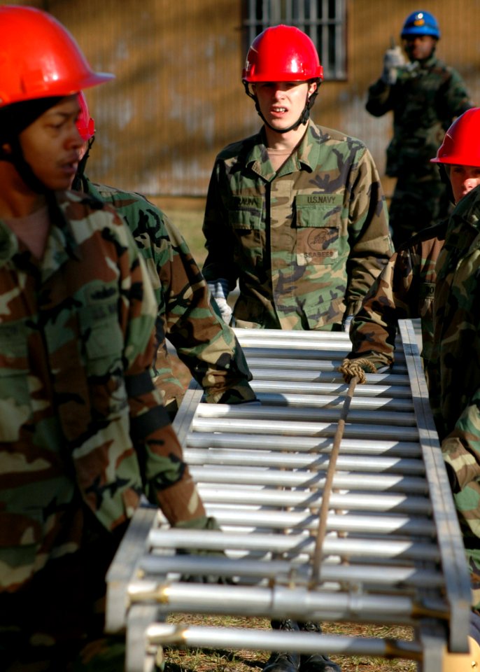 US Navy 070126-N-3857R-001 Builder Constructionman Michael Braun, center, assigned to Naval Mobile Construction Battalion One (NMCB-1), helps carry a ladder to be used to access the roof of a training structure so rescuers may