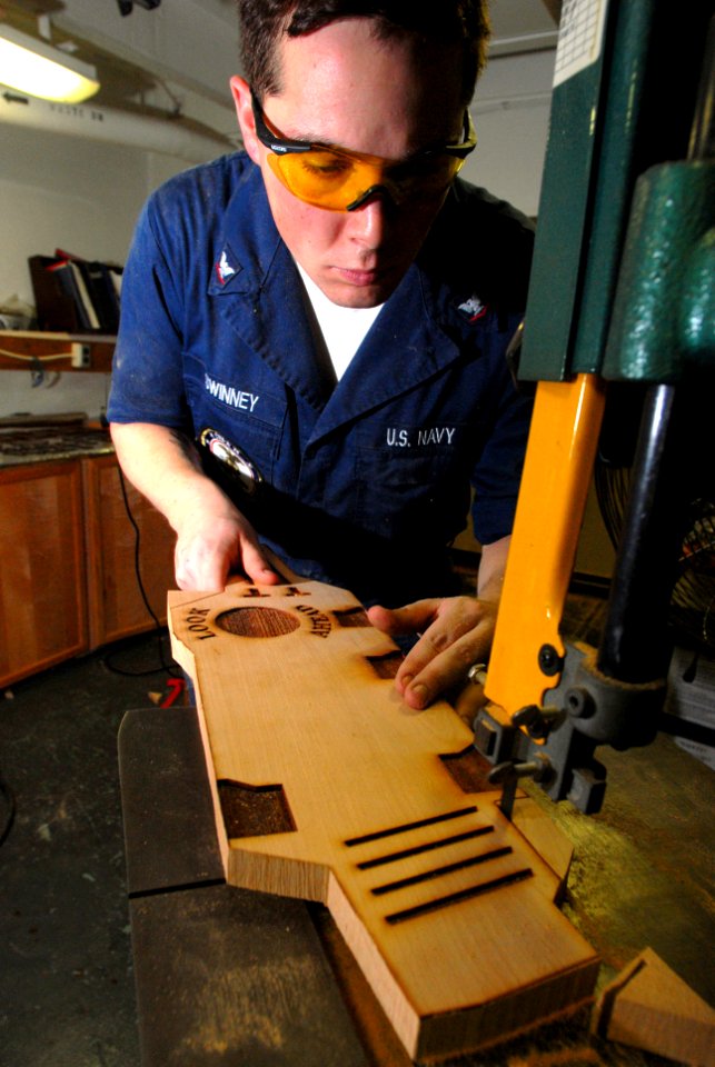 US Navy 070131-N-2659P-168 Hull Technician 3rd Class Greg Swinney uses a band saw to cut out a wooden aircraft carrier shaped ceremonial coin board in the carpentry shop aboard Nimitz-class aircraft carrier USS John C. Stennis