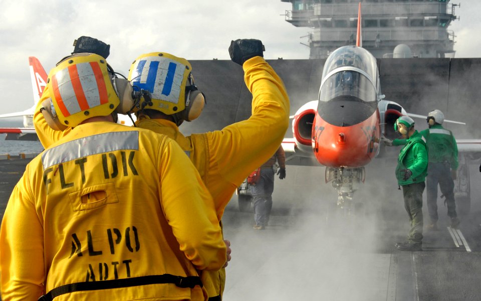 US Navy 070201-N-8923M-077 An aircraft director-in-training signals for the pilot of a T-45 Goshawk trainer to come to rest while staging for launch during flight operations on board Nimitz-class aircraft carrier USS Harry S. T