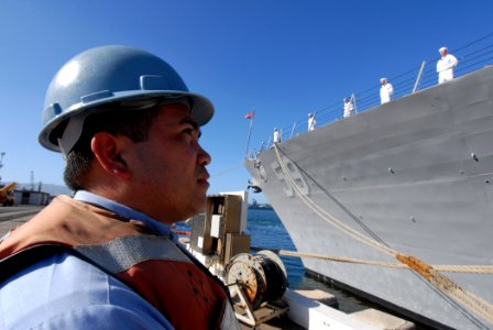 US Navy 070203-N-4965F-013 A Sailor assigned to Naval Station Pearl Harbor waits to let out mooring lines as Sailors aboard guided missile destroyer USS Russell (DDG 59) man the rails prior to getting underway