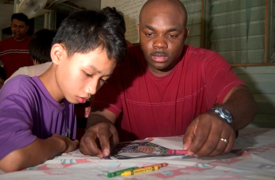 US Navy 070204-N-8534H-004 Information Systems Technician 1st Class Kufere Usanga colors a coloring book with a child of the Bukit Harap Home for Children with Special Needs and Orphanage during a visit to Malaysia