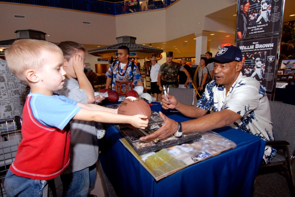 US Navy 070208-N-4965F-001 A young patron hands a football to Willie Brown, Hall of Fame cornerback for the Oakland Raiders, during an autograph signing session at the Pearl Harbor Navy Exchange