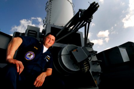 US Navy 070217-N-3729H-004 Chief Fire Controlman Walter Bayne, assigned to combat systems department's anti-ship missile division, sits next to a Phalanx Close In Weapons System (CIWS) 20mm machine gun on the flight deck aboard
