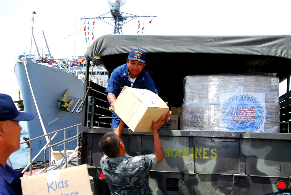US Navy 070224-N-4124C-102 Boatswain's Mate 2nd Class Arvin A. Ilaccabera, assigned aboard the amphibious transport dock USS Juneau (LPD 10), is assisted by a member of the Philippine navy in loading Project Handclasp mat