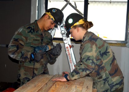 US Navy 070302-N-6247M-007 Engineering Aid Constructionman Alex Bobinger, from Snohomish, Wash., and Utilitiesman 3rd Class Elizabeth Voegtlin, from Biloxi, Miss., drill eye lip screws into a two-by-four in preparation of makin photo