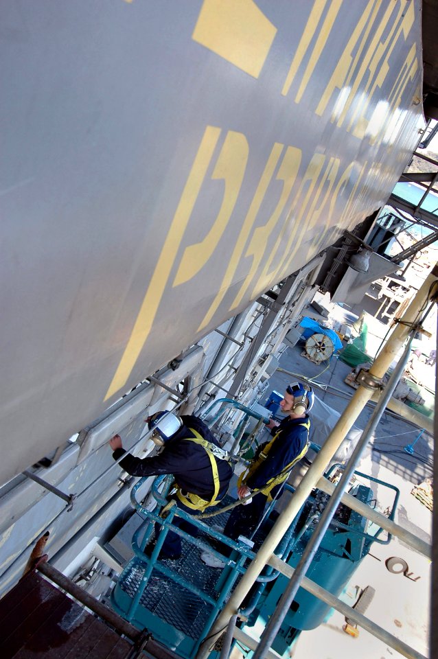 US Navy 070312-N-7883G-111 Airman Gilene Lopez from Carson, Calif., and Airman Ryan Waterbury from Llano, Texas, use a cherry picker to prepare the island of USS Kitty Hawk (CV 63) for painting