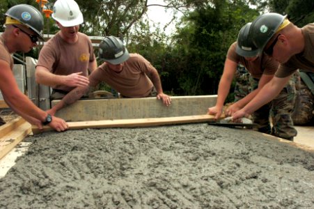 US Navy 070416-N-0775Y-004 Chief Builder Aaron Gilmer supervises Seabees from Naval Mobile Construction Battalion (NMCB) 3 as they use a two-by-four to level concrete during the construction of a storage facility at Camp Hansen