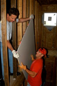US Navy 070502-N-9604C-001 Two Sailors maneuver a piece of sheetrock through an unfinished wall during a Habitat for Humanity community relations project