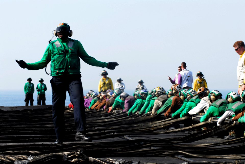 US Navy 070512-N-3729H-076 Aviation Boatswain's Mate (Equipment) 3rd Class Trevino Crowder directs flight deck personnel working together to rig the aircraft barricade aboard the Nimitz-class aircraft carrier USS John C. Stenni