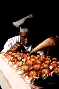 US Navy 070516-N-3729H-006 Culinary Specialist 3rd Class Ugene Ward applies frosting and fresh strawberries to one of many cakes made to serve approximately 5,000 Sailors and Marines photo