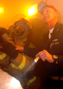 US Navy 070523-N-5928K-008 Ship's Fire Marshall, Chief Warrant Officer Jeff Lomax, instructs a nozzle man on proper fire fighting techniques during a simulated fire in the jet shop during a general quarters