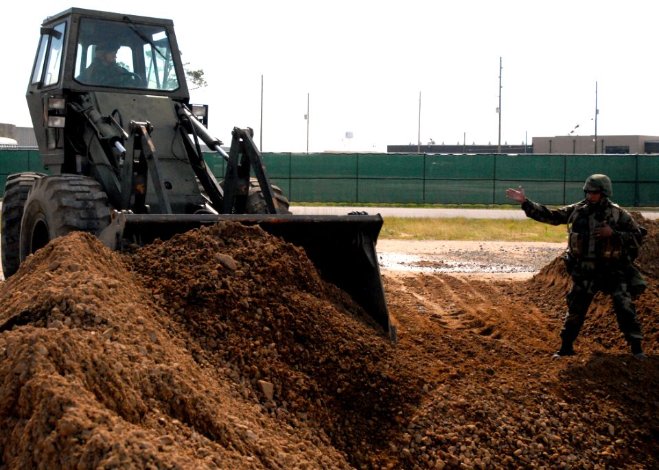US Navy 070605-N-7367K-006 Equipment Operator 1st Class Edwin Ortiz, assigned to Naval Mobile Construction Battalion (NMCB) 1 Seabee, guides a front-end loader to fill a hole in a simulated runway