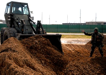 US Navy 070605-N-7367K-006 Equipment Operator 1st Class Edwin Ortiz, assigned to Naval Mobile Construction Battalion (NMCB) 1 Seabee, guides a front-end loader to fill a hole in a simulated runway photo