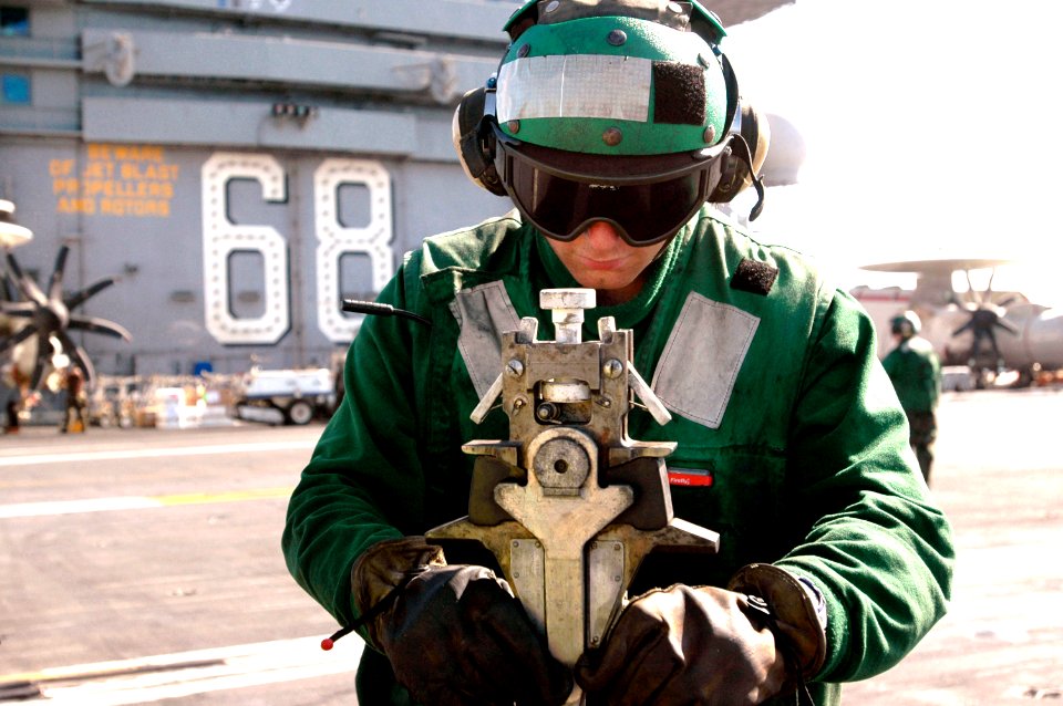 US Navy 070605-N-8119R-022 Aviation Boatswain's Mate Equipment 3rd Class Matthew Young performs a maintenance check on a holdback bar before flight operations on the flight deck of the nuclear-powered aircraft carrier USS