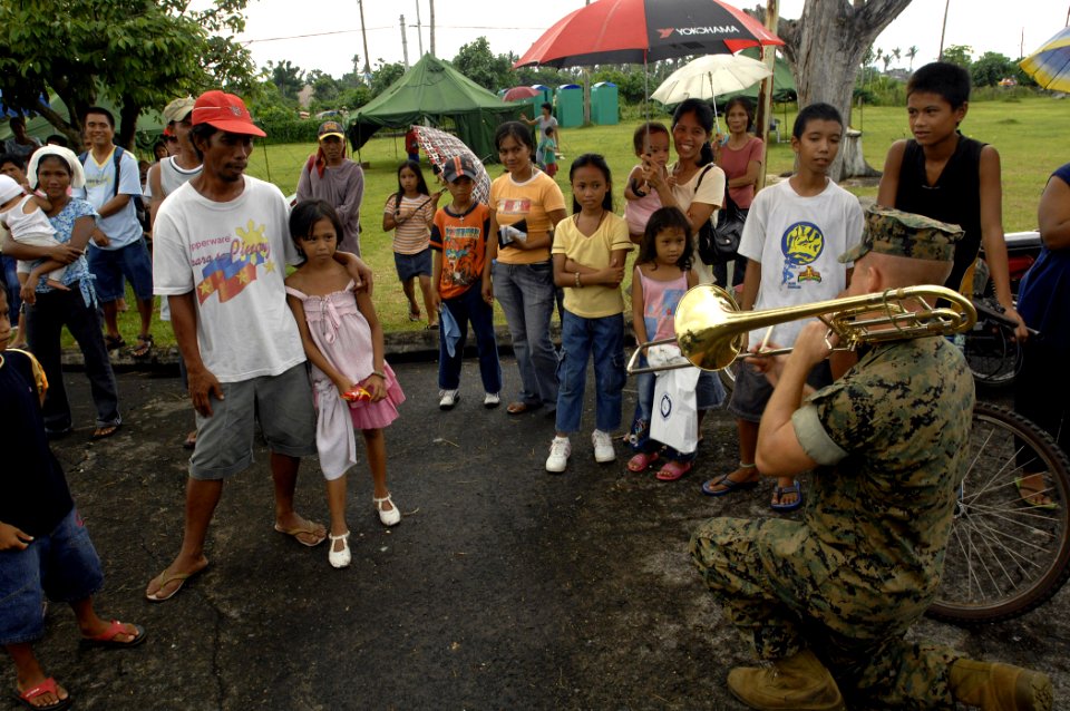 US Navy 070623-N-4954I-313 Cpl. Zachary Wendt, with the U.S. Marine Corps Forces Pacific Band, kneels down in front of a Filipino family and plays his trombone at Ziga Memorial Hospital