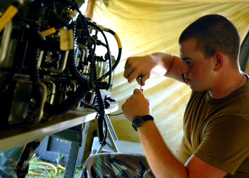 US Navy 070620-N-3857R-001 Personnel Specialist 3rd Class Ray Guedry, of Naval Mobile Construction Battalion (NMCB) 1, splices a communications wire in the ant farm of the battalion's forward operating base (FOB) during Operati