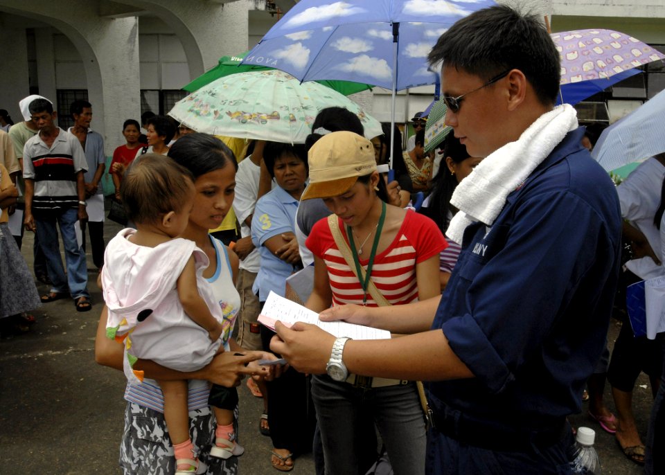 US Navy 070623-N-4954I-174 Aviation Boatswain's Mate (Handling) 3rd Class John Paul Onglatco, attached to amphibious assault ship USS Peleliu (LHA 5), reviews medical paperwork for a Filipino mother and her daughter in front of