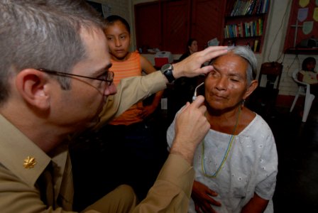 US Navy 070623-N-8704K-042 U.S. Navy Lt. Cmdr. Brian Hatch, attached to the Military Sealift Command hospital ship USNS Comfort (T-AH 20), performs eye care for Nicolasia Ical at the Monsignor Romero Roman Catholic School photo