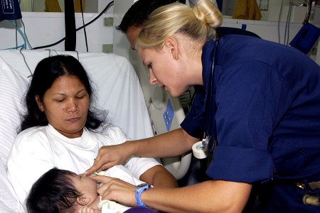 US Navy 070701-N-9421C-031 Ensign Stacy Syrstad checks the stitches of young cleft palette patient in the recovery room aboard amphibious assault ship USS Peleliu (LHA 5)