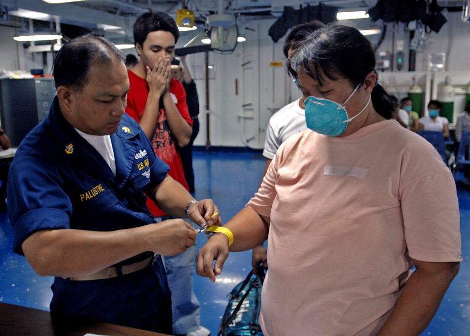 US Navy 070629-N-4954I-015 Chief Hospital Corpsman Ron Palustre puts a medical identification bracelet on a Filipino patient as she enters the medical ward of USS Peleliu (LHA 5)