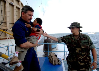 US Navy 070701-N-6278K-140 Lt. Cmdr. Karl Kish, a Navy chaplain, carries a patient into a boat for return home to Guatemala from Military Sealift Command hospital ship USNS Comfort (T-AH 20) photo