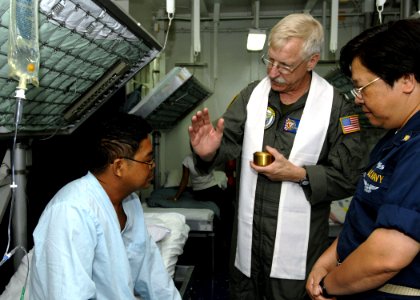 US Navy 070702-N-4954I-044 Cmdr. Jerome Dillon, the command chaplain, prepares to anoint a Filipino patient with oil as Chief Personnel Specialist Erlinda Lleva stands by to translate in the medical ward of amphibious assault s