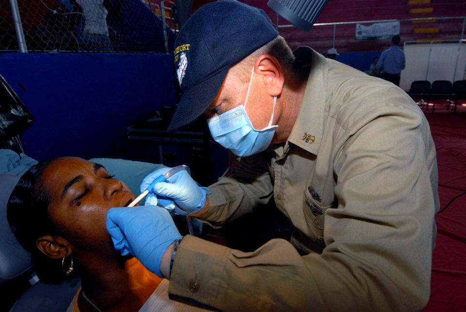 US Navy 070706-N-8704K-035 Command Master Chief Ken Day, attached to Military Sealift Command hospital ship USNS Comfort (T-AH 20), performs dental care for Saranara Chevantes at the Paul Brown Arena