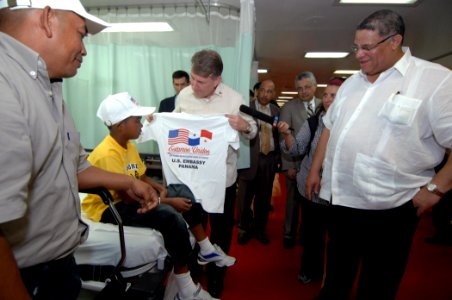 US Navy 070705-N-0194K-125 Ambassador William Eaton, U.S. ambassador to Panama, a child and his father with t-shirts as Camilo Alleyne, minister of health for Panama looks on aboard the Military Sealift Command hospital ship US