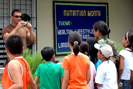 US Navy 070706-N-9421C-122 Information Systems Technician 2nd Class Donald Seaux takes a photograph of Electronics Technician 1st Class Marianne Duplon and a group of Filipino children at Gogon Elementary School