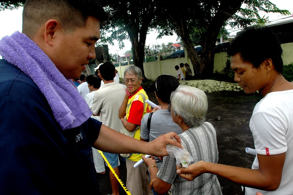US Navy 070706-N-9421C-059 Aviation Boatswain's Mate (Handling) 3rd Class Eduardo Ople shares a snack with a resident while waiting in line to be seen by the Pacific Partnership medical staff at Gogon Elementary School