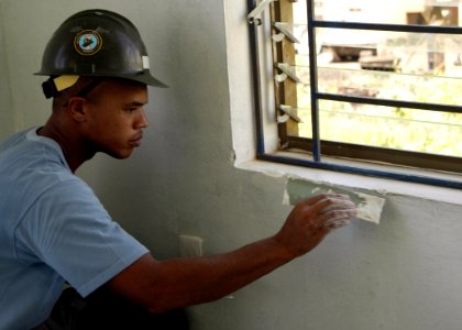 US Navy 070716-N-6999H-022 Construction Mechanic 2nd Class Josh Thomas, assigned to Amphibious Construction Battalion (ACB) 1, applies putty compound to repair a window ledge during an engineering civic action program at the Ho
