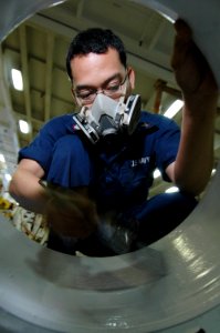 US Navy 070714-N-7883G-022 Aviation Support Equipment Technician 3rd Class Herbert Esguerra paints rims belonging to flight deck fire trucks and tractors in the ground support equipment shop aboard USS Kitty Hawk (CV 63)