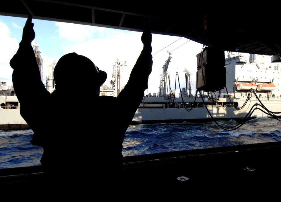 US Navy 070717-N-8923M-045 Boatswain's Mate 3rd Class Micky Nelson signals to a cable operator as cargo is passed the Military Sealift Command fleet replenishment oiler USNS Laramie (T-AO 203)