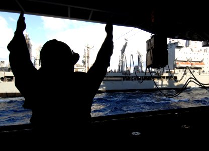 US Navy 070717-N-8923M-045 Boatswain's Mate 3rd Class Micky Nelson signals to a cable operator as cargo is passed the Military Sealift Command fleet replenishment oiler USNS Laramie (T-AO 203)