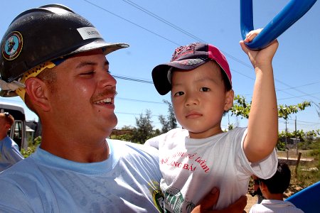 US Navy 070722-N-9421C-143 Equipment Operator 2nd Class Robert Bustos plays with a Vietnamese child on a newly built playground set at Hoi Mai Orphanage during an engineering civic action program in support of Pacific Partnersh