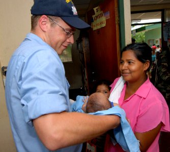 US Navy 070720-N-8704K-134 Hospitalman Wesley Williams, attached to Military Sealift Command hospital ship USNS Comfort (T-AH 20), hands an 18-day-old child back to his mother at the 15 de Julio Health Care Center