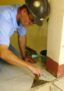 US Navy 070721-N-9195K-055 Steelworker 3rd Class Jason Tinkman of Navy Mobile Construction Battalion (NMCB) 7 lays down grout before placing floor tiles during an engineering civic action program conducted at An Khe Clinic in s photo