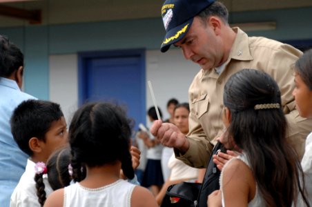 US Navy 070723-N-7088A-015 Capt. Bob Kapcio, mission commander aboard Military Sealift Command hospital ship USNS Comfort (T-AH 20), passes out pencils to children at the El Realejo Health Care Center photo