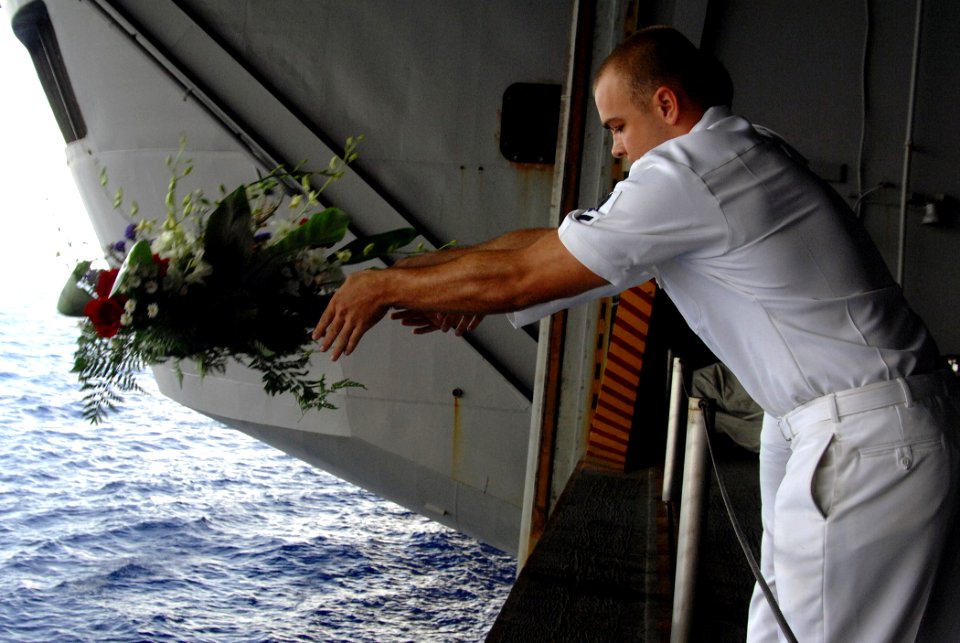US Navy 070724-N-8923M-121 Aviation Machinist's Mate 3rd Class Robert Scott, from the Raging Bulls of Strike Fighter Squadron (VFA) 37, tosses a wreath overboard in honor of Aviation Ordnanceman 3rd Class Adam Cline