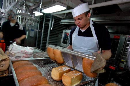 US Navy 070728-N-7883G-017 Culinary Specialist Seaman Alberto Guillen places bread on cooling racks in USS Kitty Hawk (CV 63) bakeshop photo