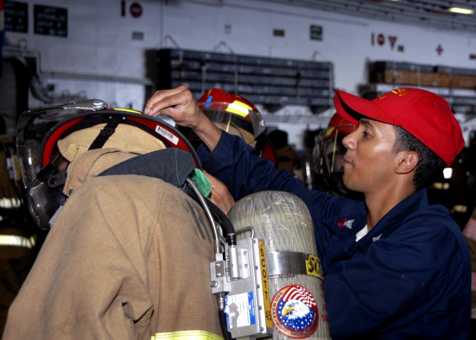 US Navy 070801-N-6410J-072 Boatswain's Mate 1st Class Saintrious Bonnet, damage control team trainer, helps a Sailor don firefighting gear during a general quarters drill