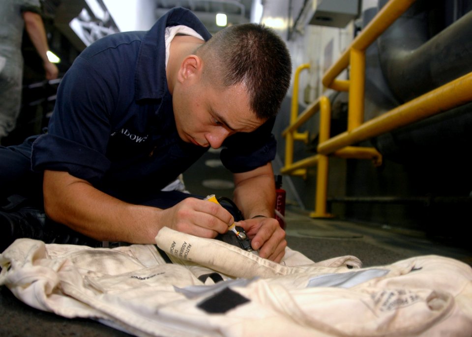 US Navy 070730-N-1226D-012 Seaman Duncan Meadows uses anti-sabotage compound to seal a nut attached to the actuator on a life vest aboard amphibious assault ship USS Bonhomme Richard (LHD 6)