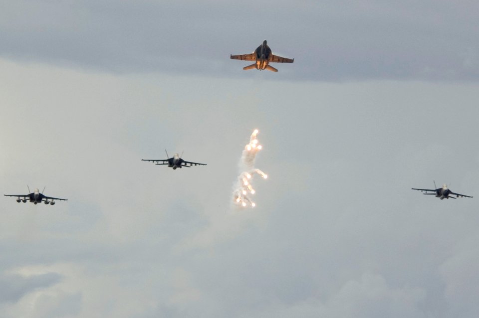 US Navy 070804-N-5387K-004 Decoy flares fall beneath an F-A-18 Hornet from the Strike Fighter Squadron (VFA) 27 during an aerial change of command over USS Kitty Hawk (CV 63)