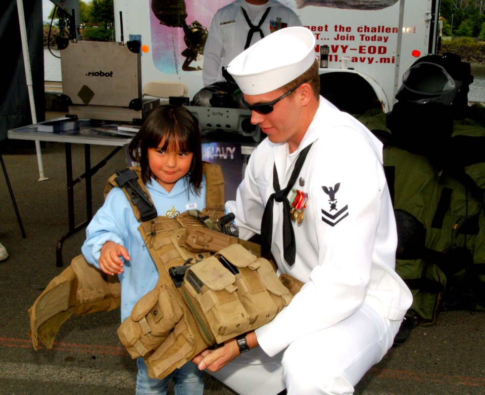 US Navy 070804-N-7783B-003 Explosive Ordnance Demolitionman 2nd Class (EOD) Edwin Gless helps put an equipment vest on a young visitor to the units display booth during a recruiting presentation at Seafair's fleet week