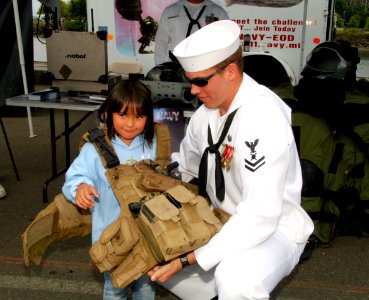 US Navy 070804-N-7783B-003 Explosive Ordnance Demolitionman 2nd Class (EOD) Edwin Gless helps put an equipment vest on a young visitor to the units display booth during a recruiting presentation at Seafair's fleet week