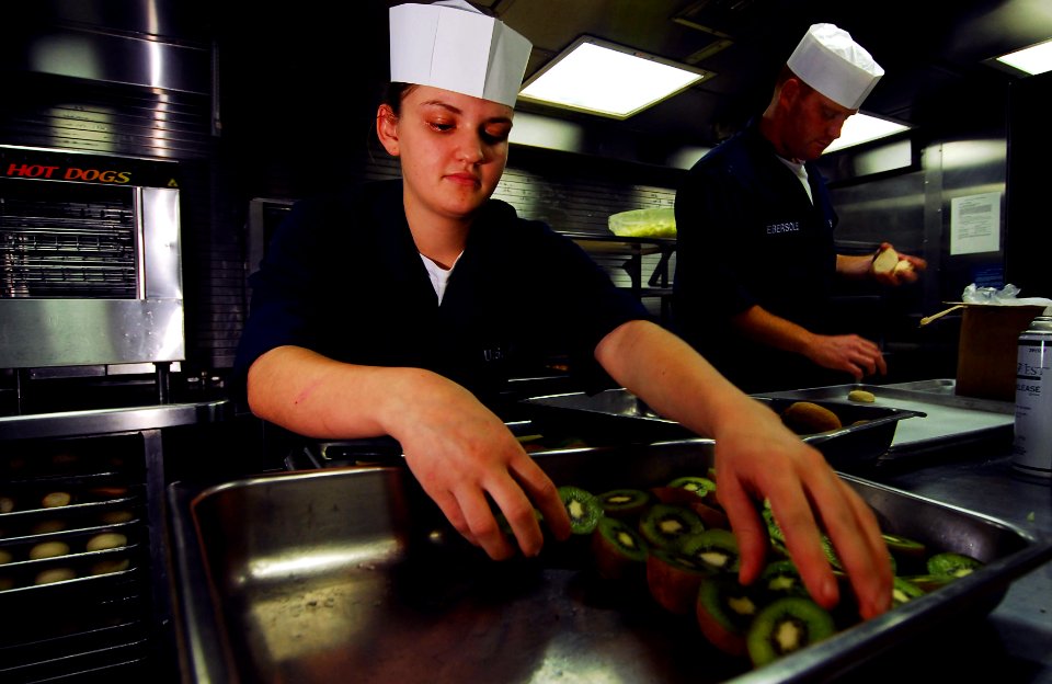 US Navy 070808-N-0684R-014 Sailors slices kiwi and place cookie dough onto baking sheets in the enlisted galley aboard the guided missile destroyer USS Preble (DDG 88)