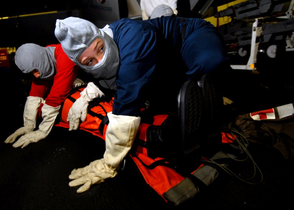 US Navy 070804-N-7981E-195 Hospital Corpsman 2nd Class Jessica Hall and members of her stretcher bearer team brace for shock while protecting a simulated casualty in the hangar bay of Nimitz-class aircraft carrier USS Abraham L