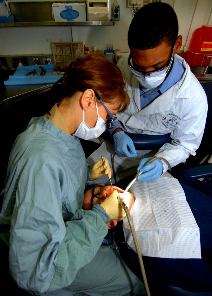 US Navy 070818-N-9898L-017 Cmdr. Nevanna Koicheff and Hospital Corpsman 2nd Class Ephlius Cornelious perform a crown delivery on Machinist's Mate 2nd Class Christina Gillen in the dental office on board USS Abraham Lincoln (CVN