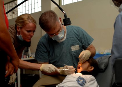US Navy 070816-N-7088A-088 Air National Guard Senior Airman Holly Moore, assists Navy Capt. Joseph Rusz, both attached to Military Sealift Command hospital ship USNS Comfort (T-AH 20), as he performs dental work on a young pati